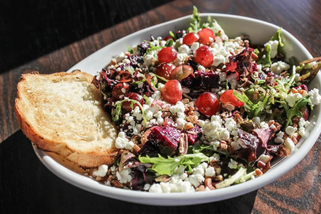 Salad with leafy greens, feta, red grapes, and bread on wood.