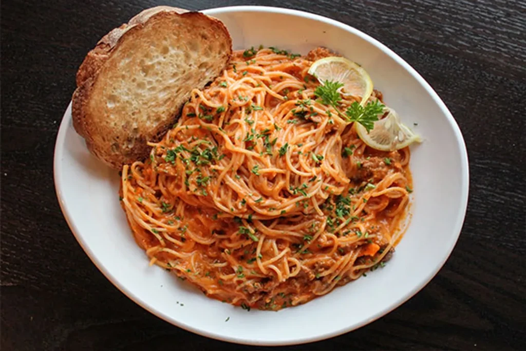Spaghetti with creamy meat sauce, bread, lemon, and herbs.