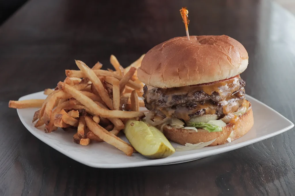 Double cheeseburger, french fries, and pickle spear on a white plate.
