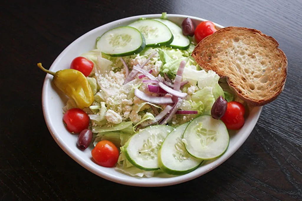 Fresh salad with lettuce, tomatoes, feta, olives, pepperoncini, and toasted bread.