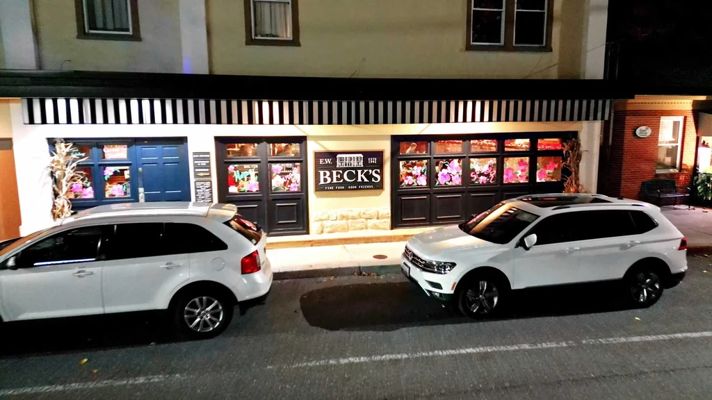E.W. Beck's restaurant at night with warm lights and two parked SUVs.