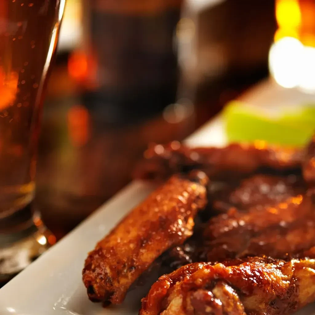 Glistening reddish-brown chicken wings on a plate with beer.