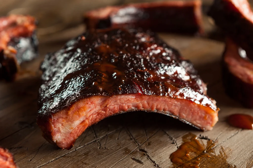 Glistening dark barbecue ribs on a rustic wooden board.
