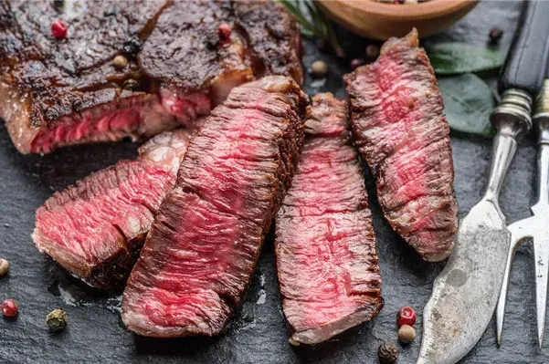 Sliced medium-rare steak with seared crust, peppercorns, knife, and herbs.