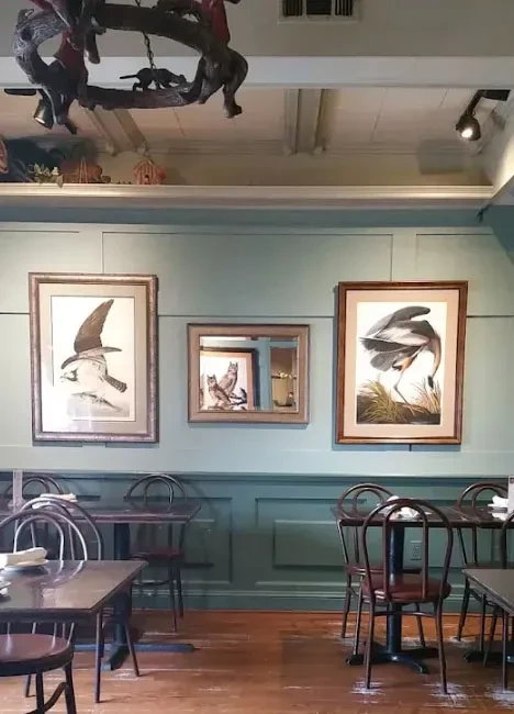 Empty dining room with green walls, nature art, rustic wood chandelier.