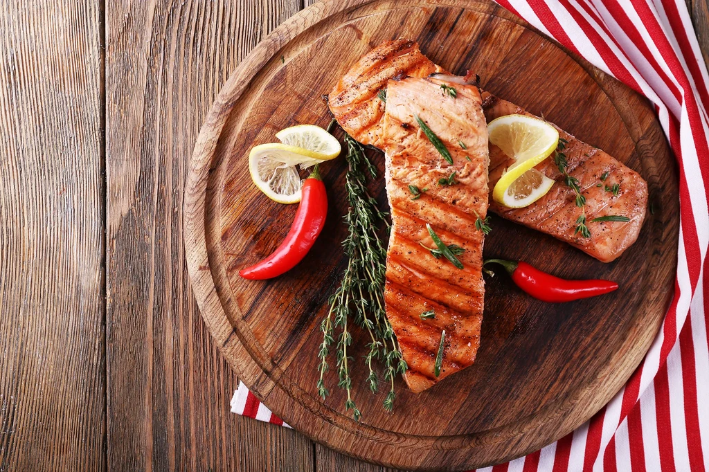 Overhead shot of two grilled salmon fillets with lemon, herbs, and chilies.