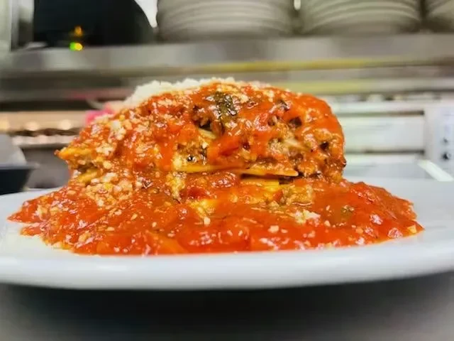 Single lasagna serving on white plate, red tomato sauce, grated cheese.