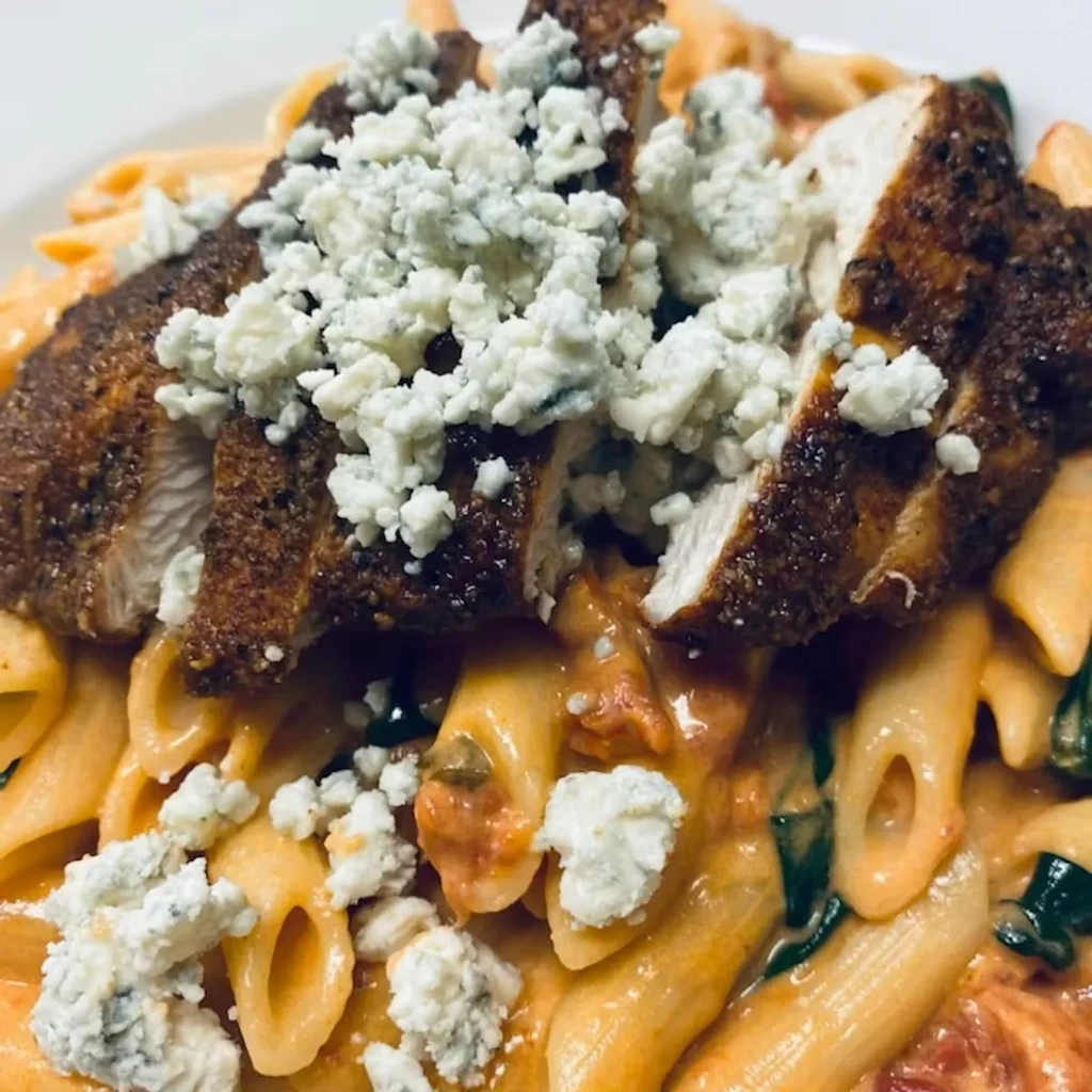 Close-up: Sliced chicken, penne pasta, creamy sauce, tomatoes, and blue cheese.