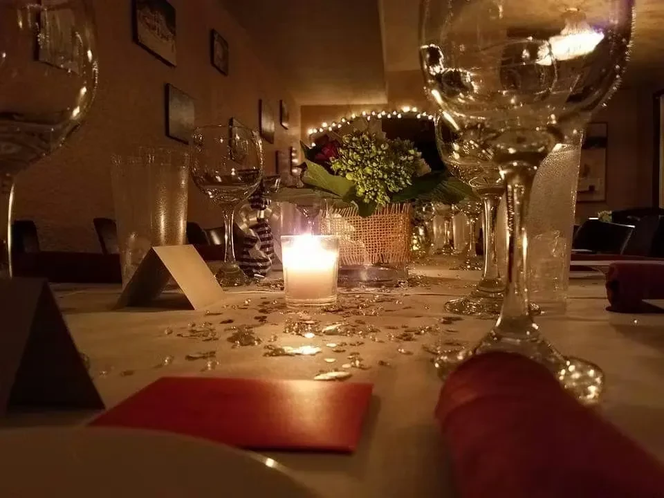 Restaurant table set with candle, wine glasses, flowers, and gold confetti.