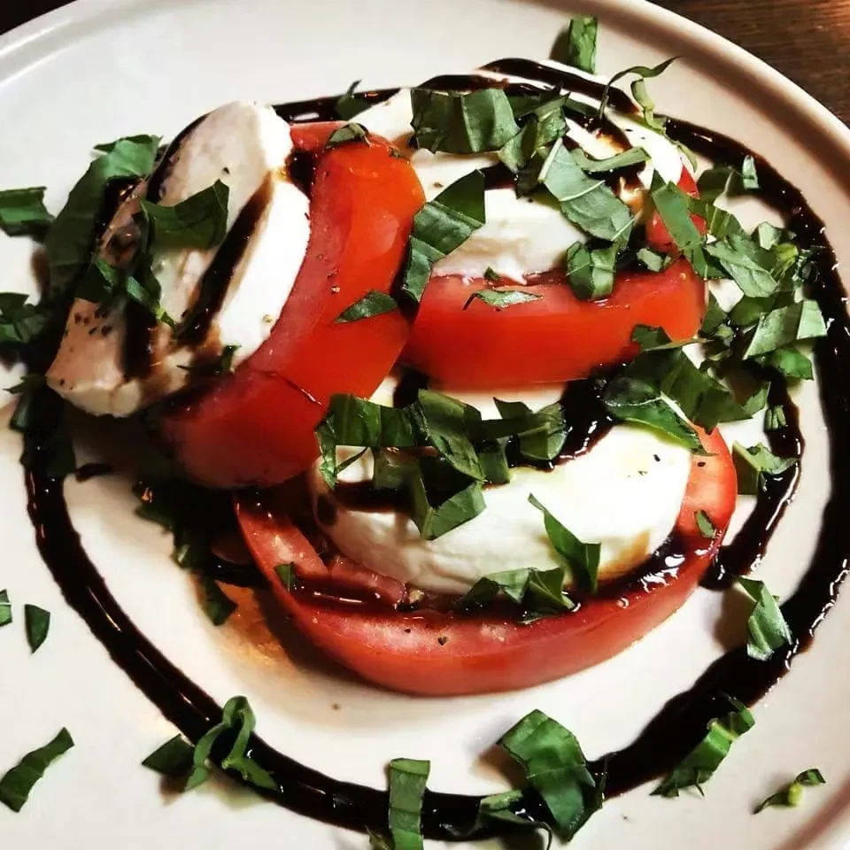 Close-up of Caprese salad with tomatoes, mozzarella, basil, balsamic glaze.