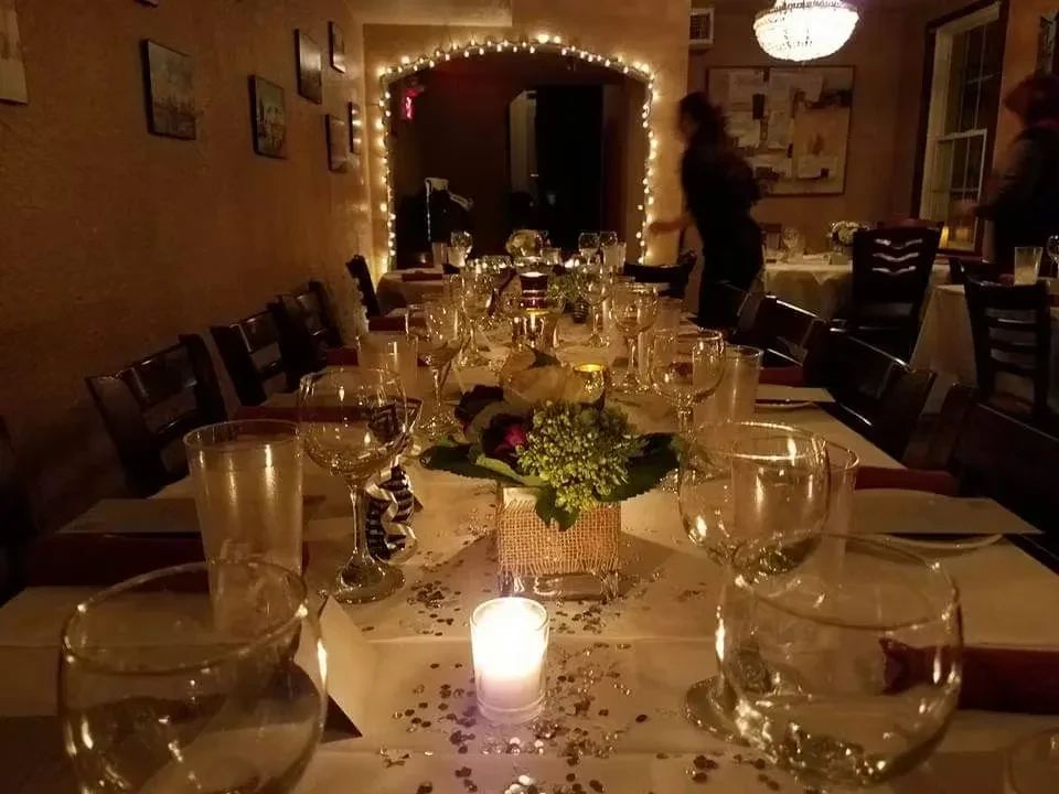 Elegantly set dining table with candles, floral centerpiece, and blurry people.
