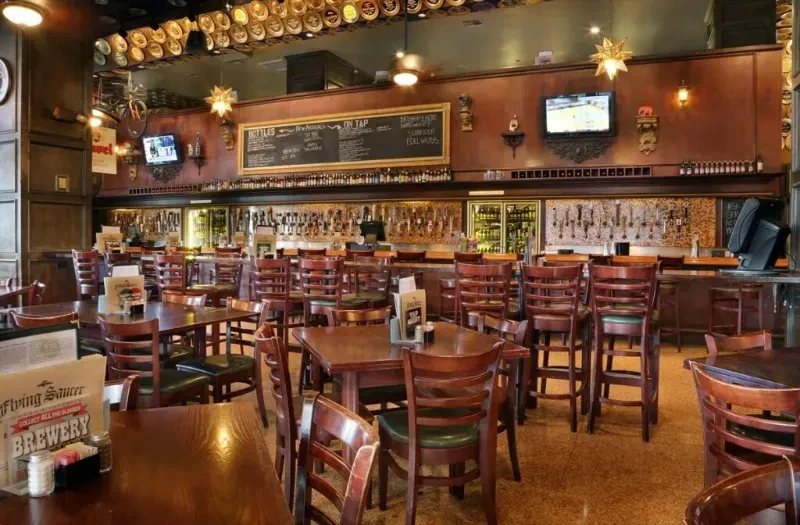 Warm brewpub interior with wooden tables, a long bar, and blackboard menu.