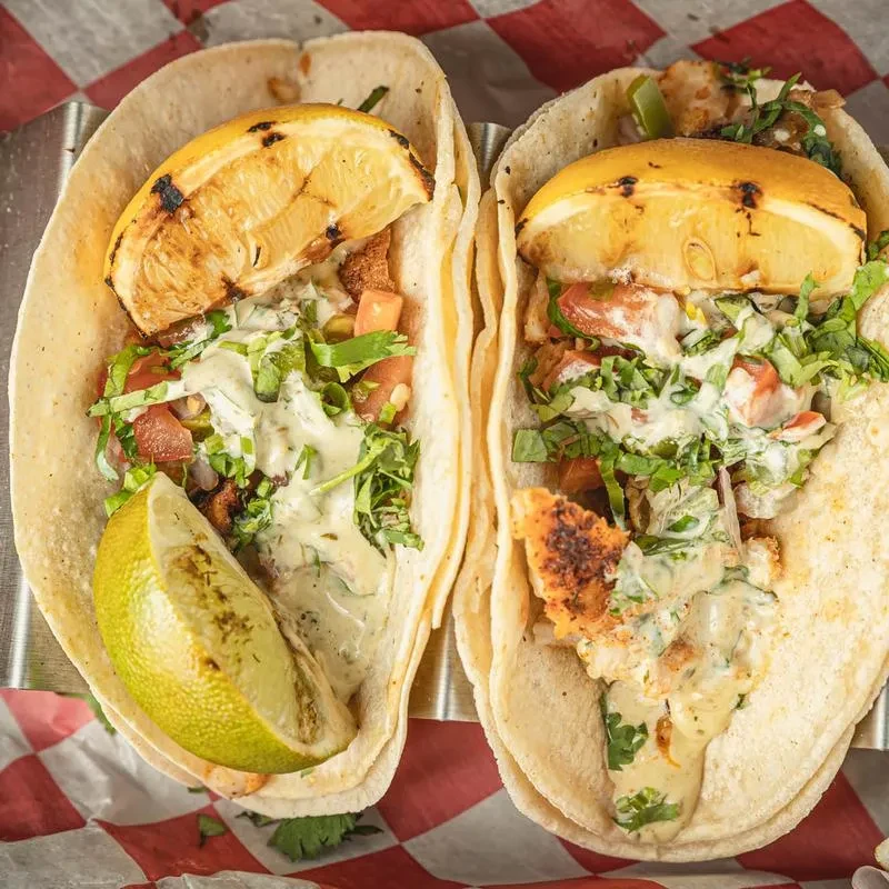 Two tacos filled with protein and vegetables, garnished with grilled lemons.