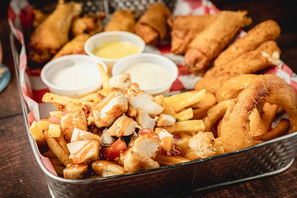 Metal tray with loaded fries, onion rings, chicken, and dipping sauces.