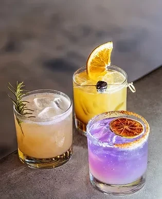 Three vibrant cocktails in short glasses, garnished, on a grey surface.