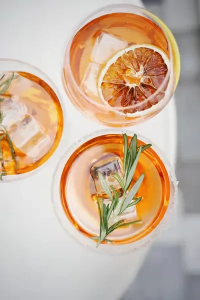 Three amber cocktails with ice; two garnished with citrus and rosemary.