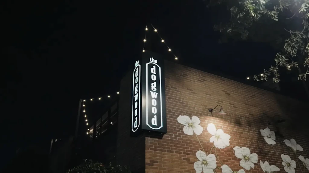 Night view of an illuminated "the dogwood" sign on a brick wall.