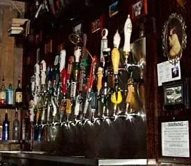 Numerous beer taps, framed pictures, and books adorn a dimly lit bar.