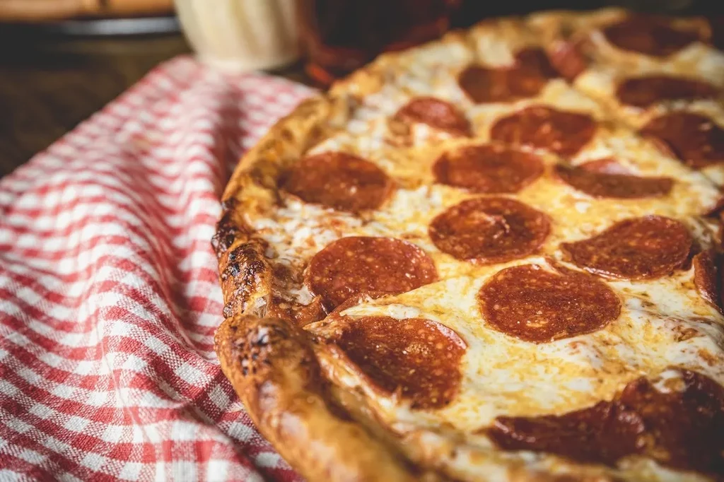 Close-up of a pepperoni pizza on a red and white checkered cloth.
