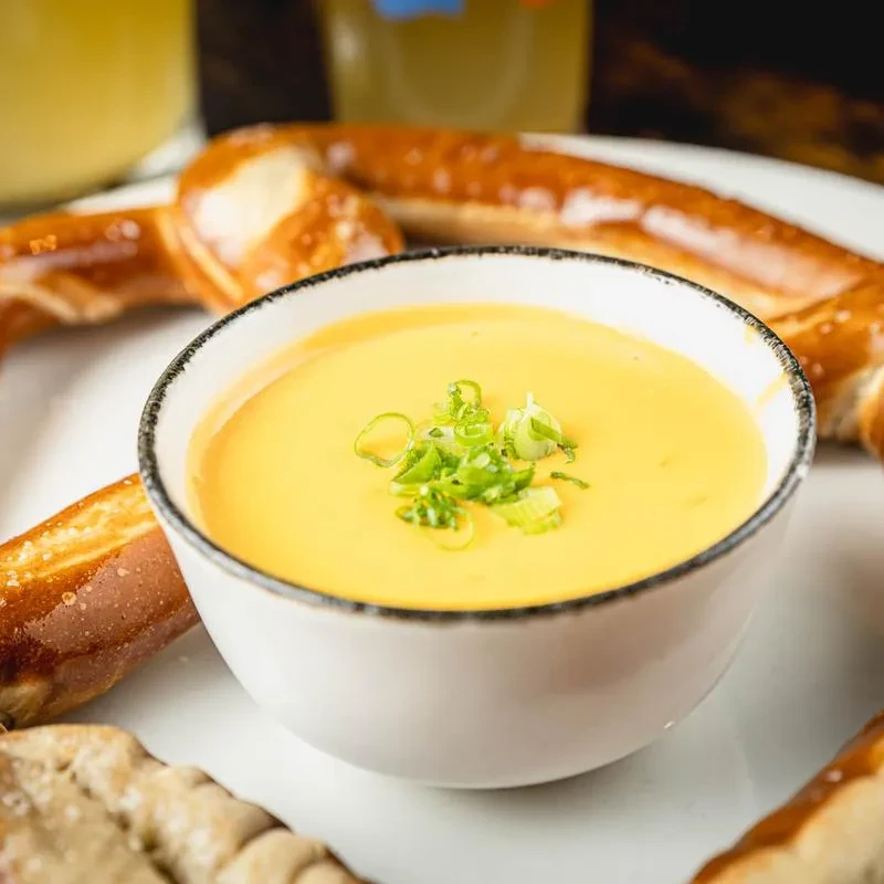 Bowl of cheese sauce with green onions and soft pretzels.
