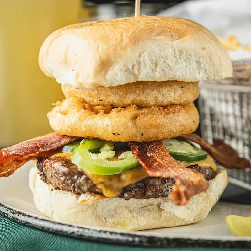 Gourmet burger with onion rings, cheddar, jalapeños, and bacon.