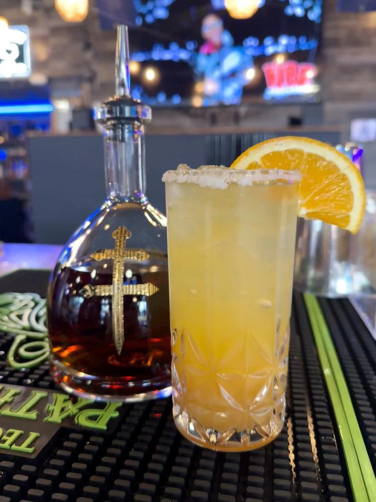 Cocktail with orange slice and spirit bottle on a bar.