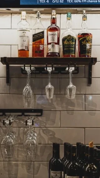 Bar area with whiskey bottles, wine glasses, and blurred screen.