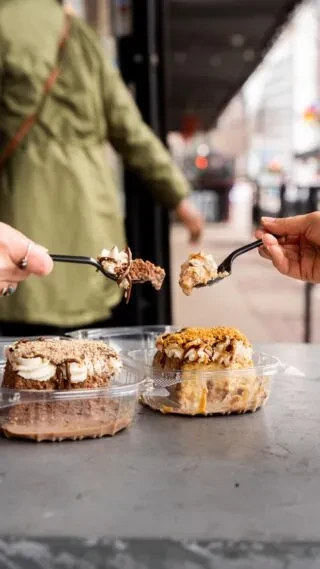 Two hands hold spoons with dessert over plastic containers.