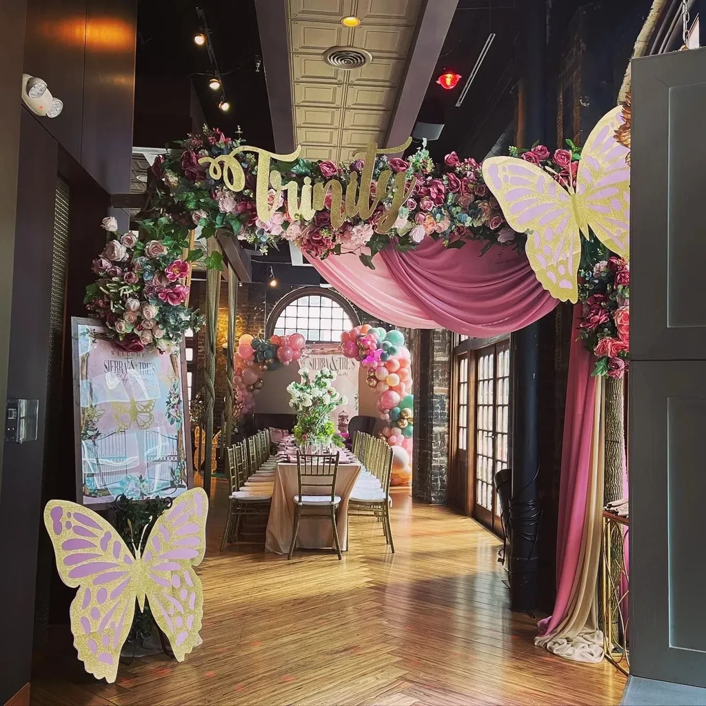 Elaborate event space with floral archway, butterfly cutouts, and dining table.