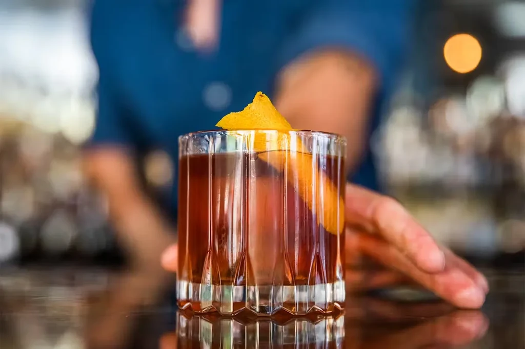 Amber drink in a ridged glass with orange peel garnish.