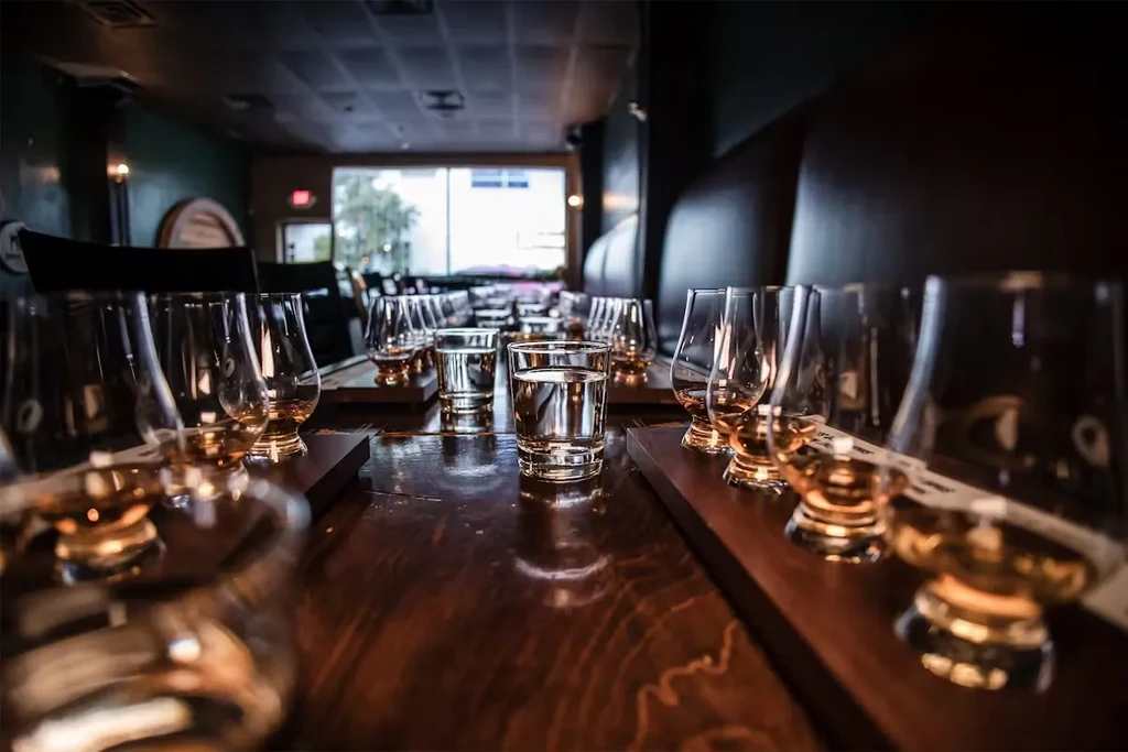 Glencairn glasses of whisky and water on wooden trays in a dim room.