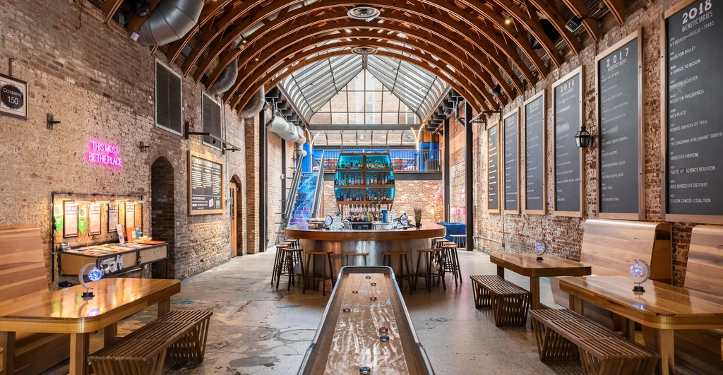 Modern industrial restaurant interior with circular bar, skylight, and shuffleboard.