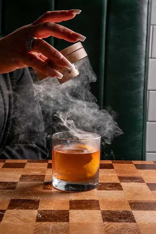 Smoke being added to an amber drink in a glass.