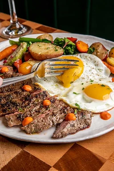 Sliced steak, fried eggs, and roasted vegetables on a white plate.