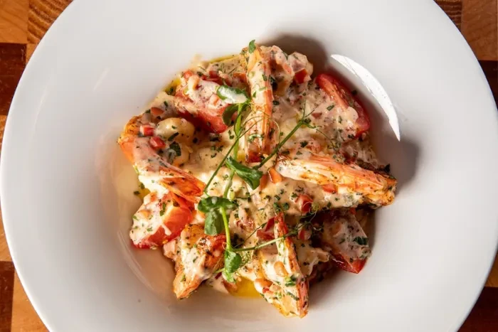 Creamy seafood dish with green herbs and red diced ingredients.