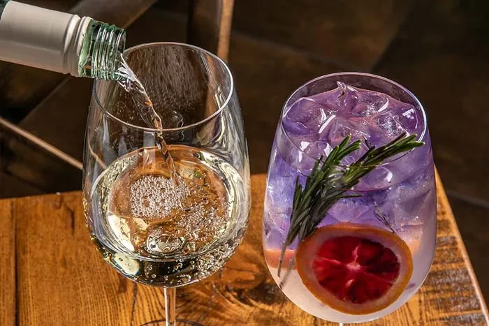 Two drinks on a wooden surface, one pouring, one garnished.