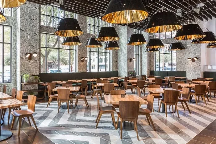Modern restaurant interior with wooden tables, banquettes, and chevron floor.