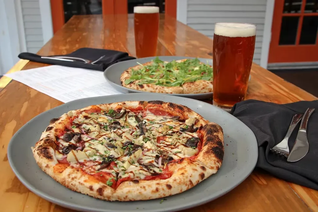 Two pizzas and two glasses of beer on a wooden table.
