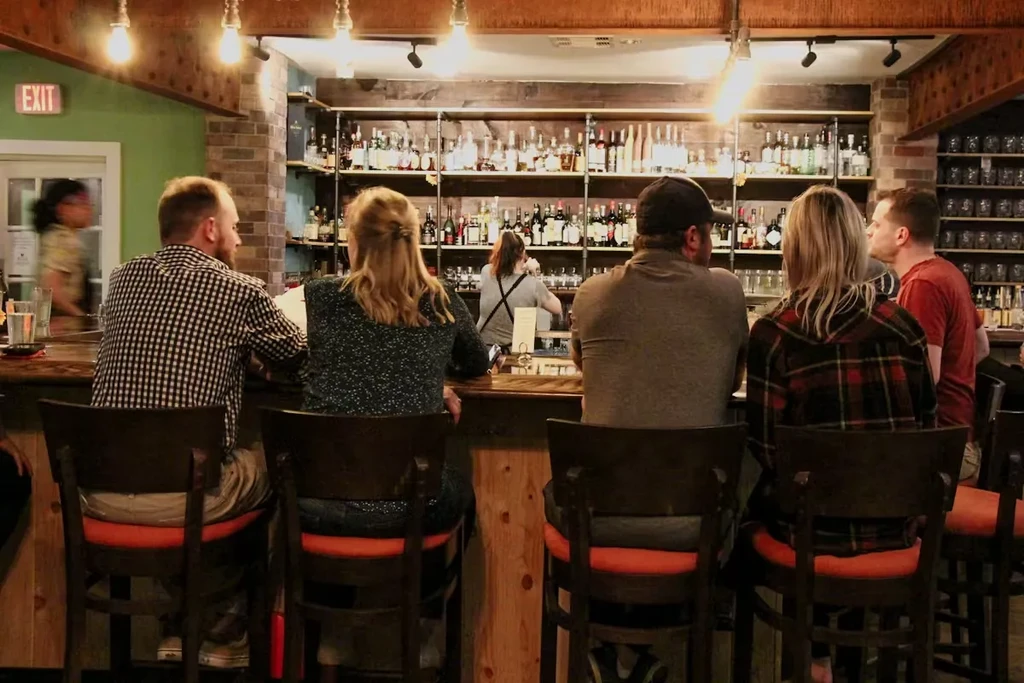 Five patrons sit at a bar with drinks and liquor display.