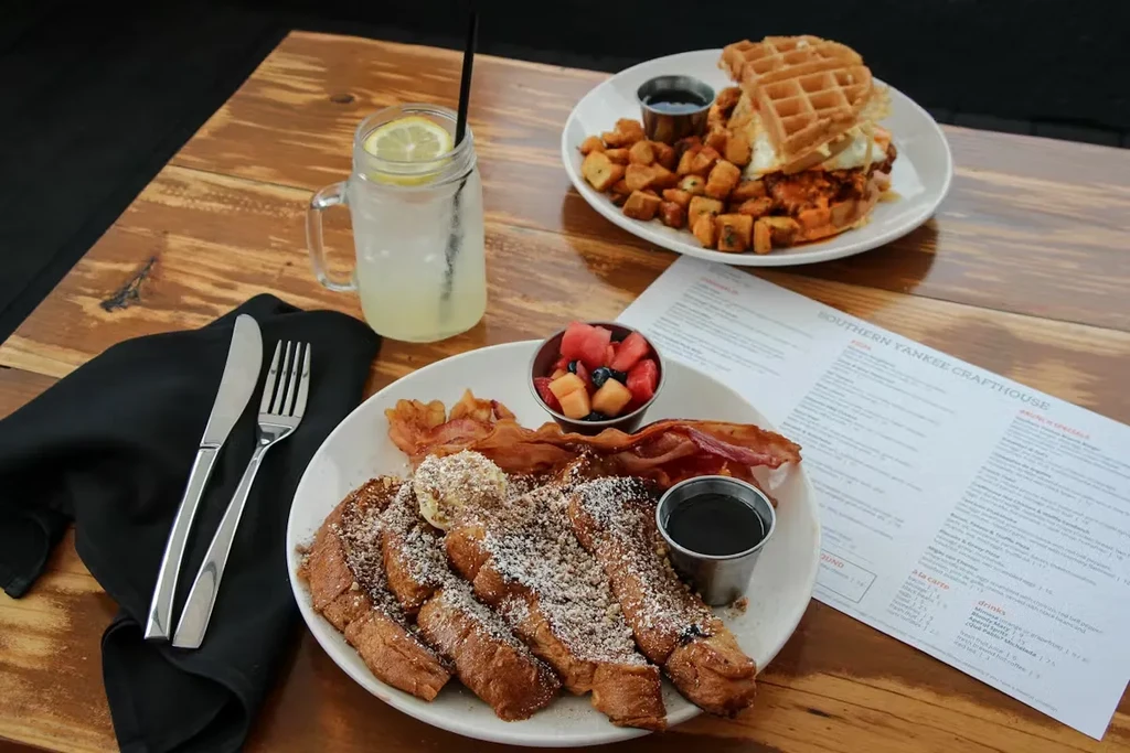 Table set with French toast, bacon, fruit, and waffle sandwich.