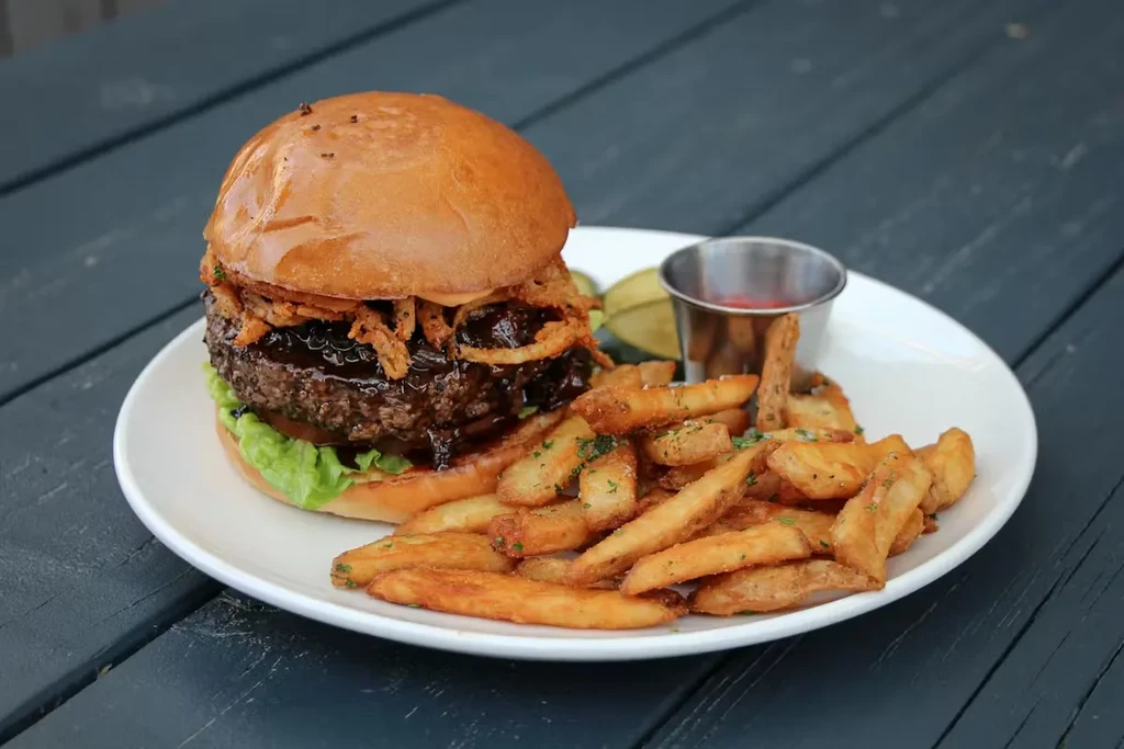 Burger and fries with ketchup and pickles on a wooden table.