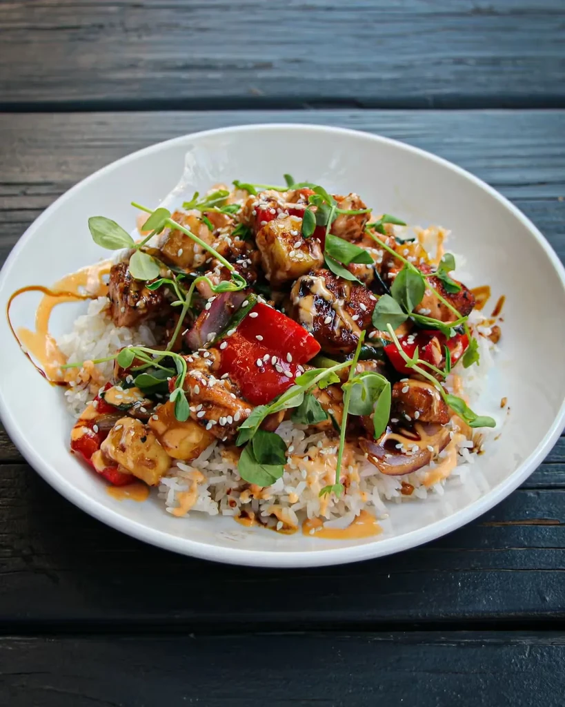 Asian-inspired dish with chicken, rice, vegetables, sprouts, and sesame seeds.
