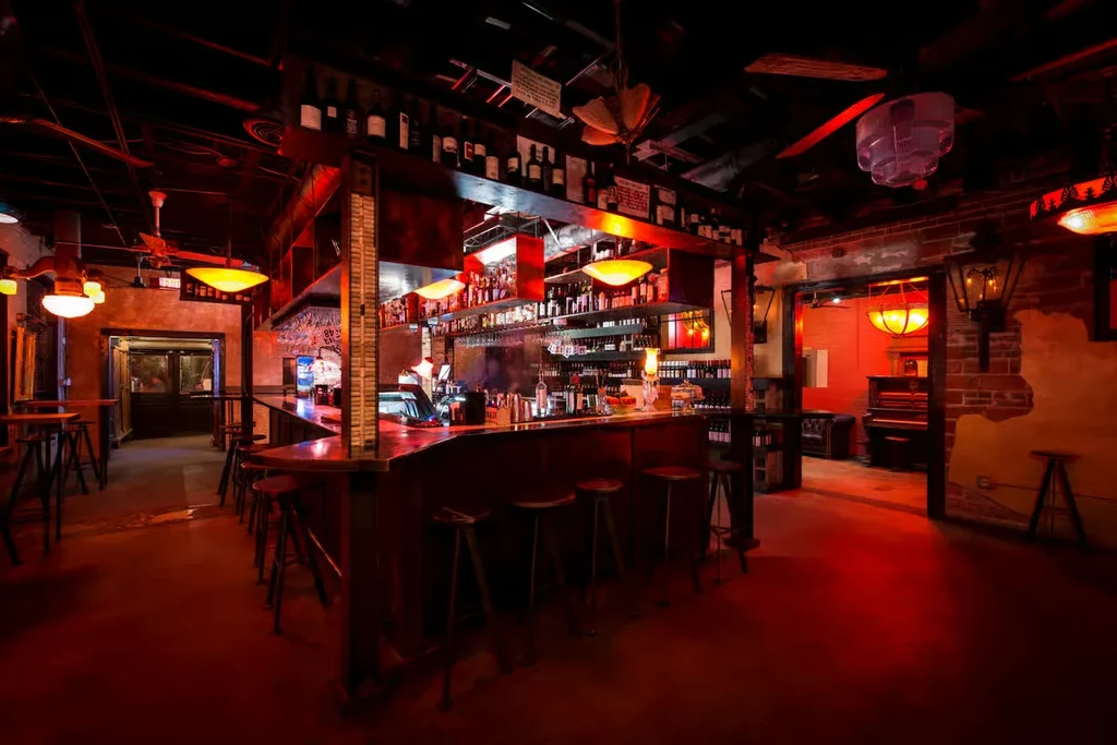 A red-lit, empty bar with bottles, glasses, and an upright piano.