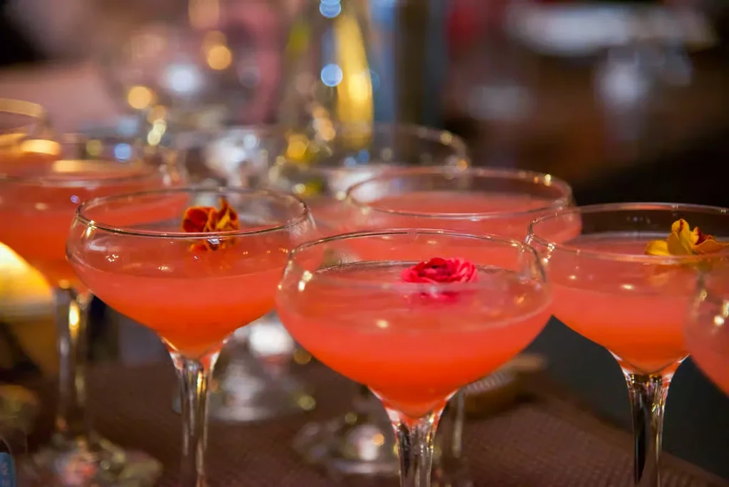 Coral-pink cocktails in coupe glasses, garnished with small flowers.