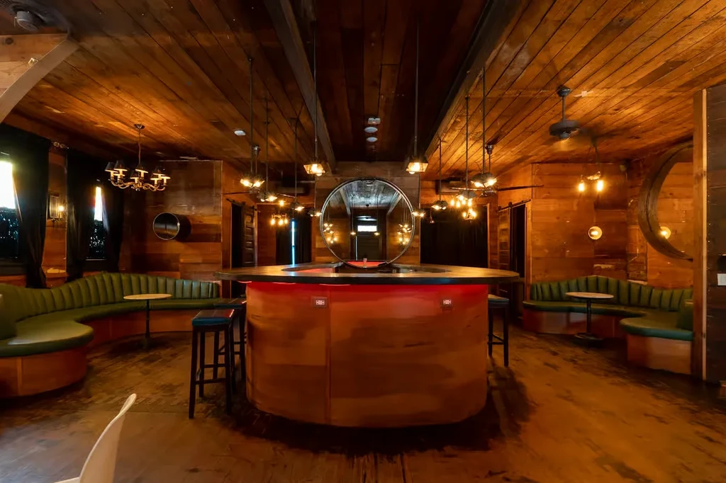 Circular bar, wooden interior, dark green booths, warm lighting.