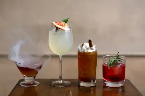Four distinct cocktails are arranged on a dark reflective surface.
