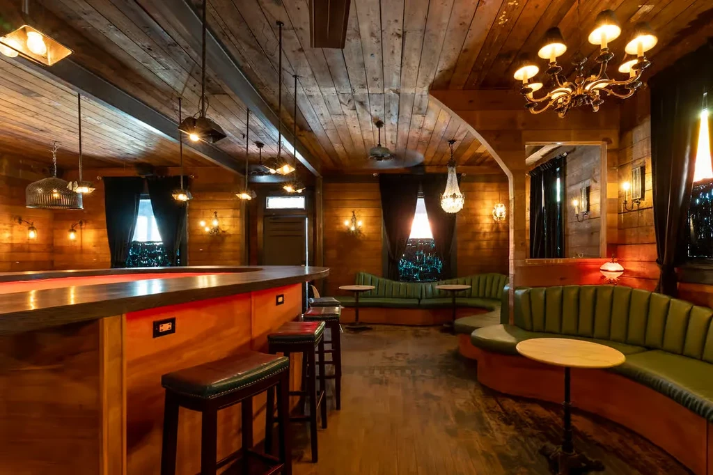 Interior of a stylish, empty bar with warm wood and green seating.