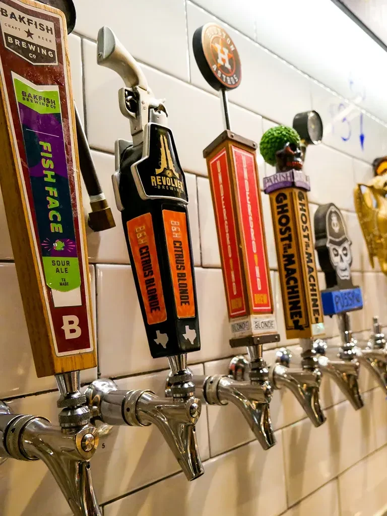 Multiple unique craft beer taps on a white subway tile wall.