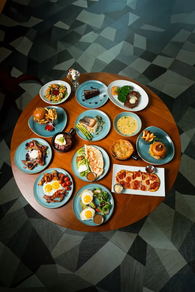 Wooden table laden with diverse breakfast, lunch, dinner, and dessert dishes.