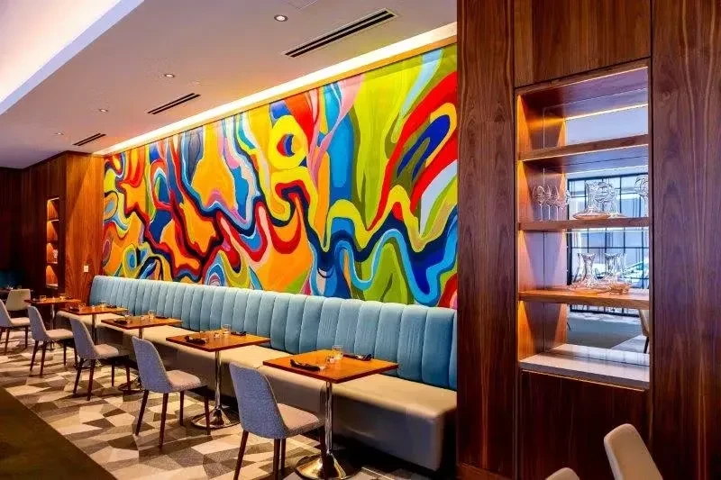 Restaurant interior with a colorful mural, booths, and wooden tables.